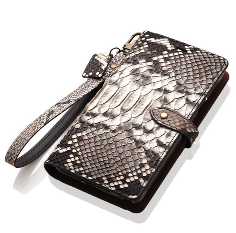 May include: A black and white snakeskin leather wallet with a wrist strap. The wallet has a flap closure and a metal clasp.