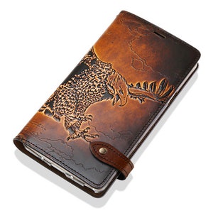 May include: A brown leather phone case with an embossed eagle design. The case has a flap that closes with a snap and a strap.
