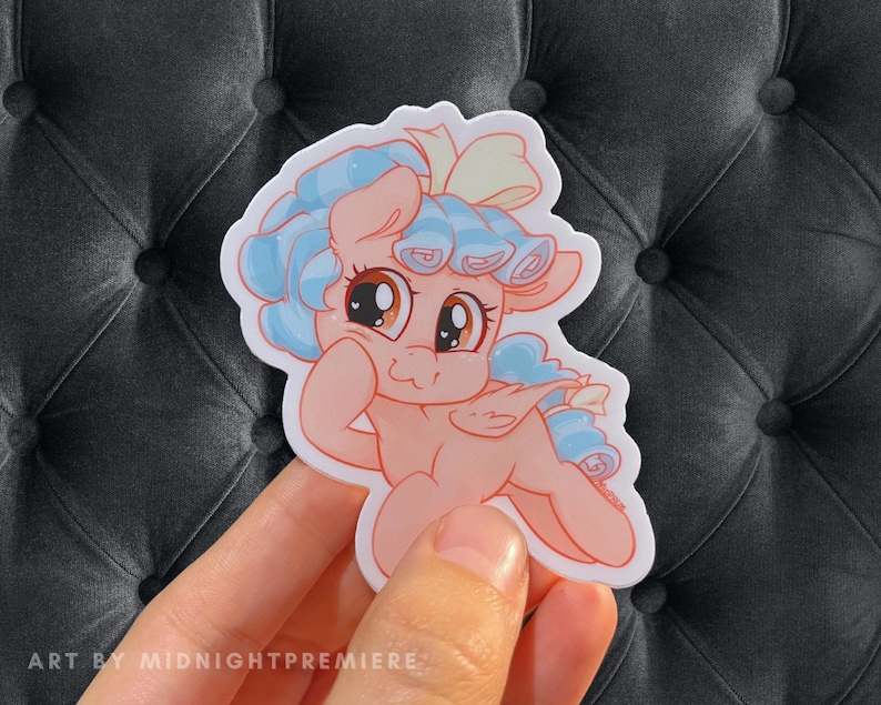 May include: A sticker featuring a cartoon pony with light blue hair, a pink body, and a white bow. The pony has large, brown eyes and a surprised expression. The sticker is on a gray background.