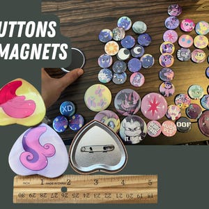 May include: A collection of colorful buttons and magnets featuring various cartoon characters and designs. The buttons are round and have a shiny finish. The magnets are heart-shaped and have a matte finish. The text "BUTTONS & MAGNETS" is visible at the top of the image.
