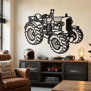 May include: A black metal wall art piece shaped like a farm tractor with large treaded tires, a steering wheel, and an exhaust pipe. The silhouette design features cutouts for the engine, seat, and wheels, creating a detailed outline of the vehicle.