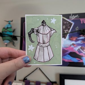 May include: A hand-drawn illustration of a stovetop espresso maker on a light green background, with white star accents. The coffee pot is in black and white, with a black handle. The artwork is on a small rectangular card.