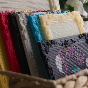 May include: A collection of rectangular pegboard frames in various colors including yellow, red, black, gray, blue, and cream. The frames feature ornate, molded edges and are arranged in a row. One black frame displays a colorful beaded design.