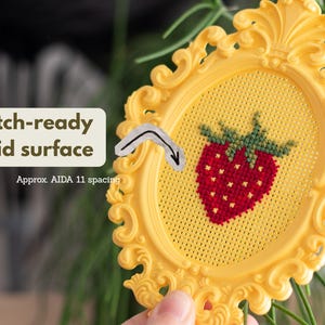 Close-up of a yellow baroque oval cross stitch frame showing the stitch-ready perforated grid with Aida 11 spacing, with a finished strawberry design. Stitchable frame printed from the STL file.