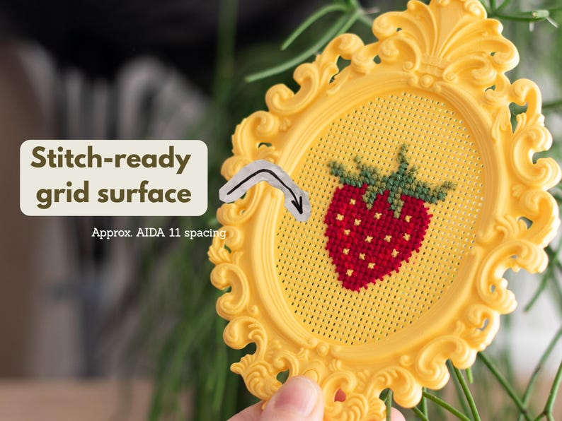 Close-up of a yellow baroque oval cross stitch frame showing the stitch-ready perforated grid with Aida 11 spacing, with a finished strawberry design. Stitchable frame printed from the STL file.