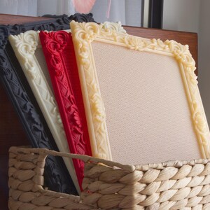 May include: Four rectangular picture frames with ornate, raised floral carvings along the borders. The frames are arranged in a row, featuring colors of black, off-white, red, and cream, each containing a textured, light-colored fabric insert.