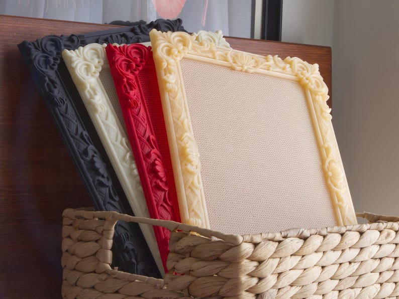 May include: Four rectangular picture frames with ornate, raised floral carvings along the borders. The frames are arranged in a row, featuring colors of black, off-white, red, and cream, each containing a textured, light-colored fabric insert.