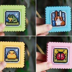 Four finished 3D printed cross stitch keepsake boxes held in hand — frog, rabbit, duck and ladybug designs stitched on perforated lids in green, blue, yellow and pink PLA