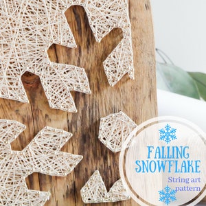 May include: String art pattern of a snowflake on a wooden board. The snowflake is made of white string wrapped around nails. The background is a light brown wood.