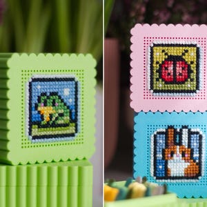 Stacked 3D printed cross stitch boxes — frog design on green box, ladybug and rabbit designs on stacked pink and blue boxes