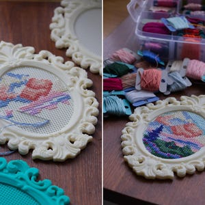 Cream baroque oval cross stitch frame with a floral design being stitched directly into the frame, shown with embroidery floss and a teal frame nearby. Stitchable frame printed from the STL file.
