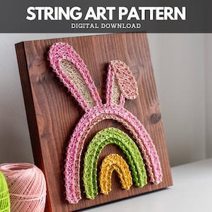 Puede incluir: Patrón de arte de cuerda de un arcoíris con orejas de conejo. El patrón está en una tabla de madera y está hecho con cuerda de colores.
