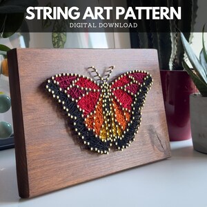 Finished butterfly string art made using digital pattern – red, orange, and black thread on wood, shown in home setting