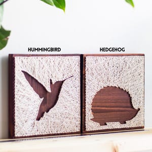 Stress relief craft kit for adults with hummingbird and hedgehog string art designs on stained wood base, relaxing DIY hobby project.