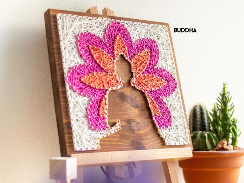 Stress relief craft kit for adults featuring Buddha silhouette with colorful string art flower design on stained wood base.