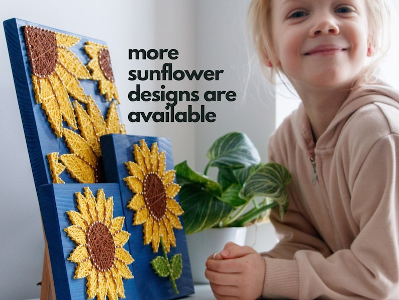 以下が含まれることがあります： ひもアートのデザインが施された木製の壁掛けが3つ。ひまわりは黄色で、中心は茶色、葉は緑色。壁掛けの背景は青色。"more sunflower designs are available"というテキストが黒地に白で書かれている。