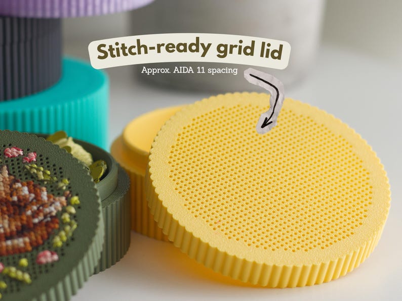 Round cross stitch box STL file — blank stitch-ready perforated lid with AIDA 11 spacing grid, shown in yellow PLA next to a green box with sleeping fawn embroidery
