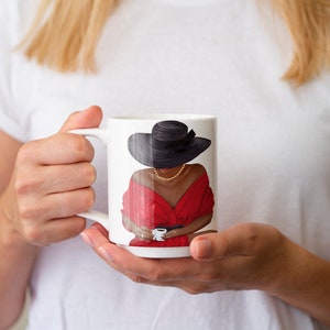 Puede incluir: Taza de cer&aacute;mica blanca con una ilustraci&oacute;n colorida de una mujer con un vestido rojo y un sombrero negro, sosteniendo una taza.