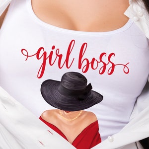 Puede incluir: Camiseta blanca de tirantes con el texto "girl boss" en letra cursiva roja. Una mujer con un sombrero negro y un vestido rojo es parcialmente visible detr&aacute;s del texto.
