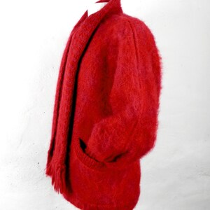May include: A red fuzzy cardigan with a matching scarf. The cardigan has a shawl collar and a pocket on the left side.