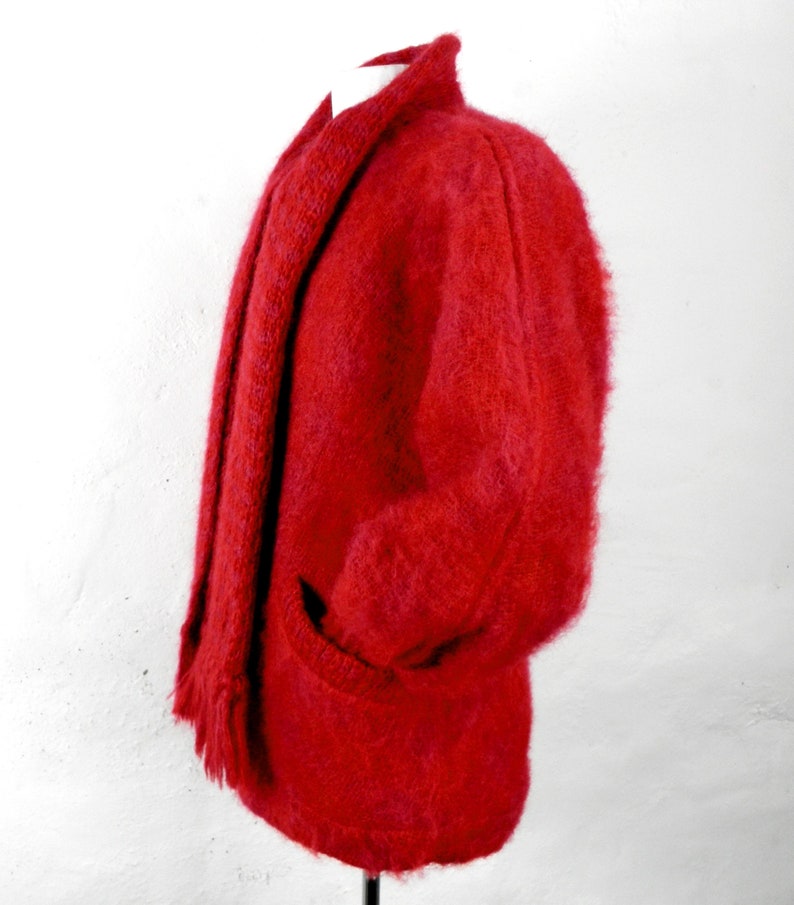 May include: A red fuzzy cardigan with a matching scarf. The cardigan has a shawl collar and a pocket on the left side.