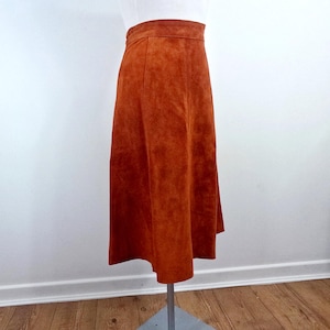 May include: A long, rust-coloured suede skirt with a high waist and a straight, A-line silhouette.