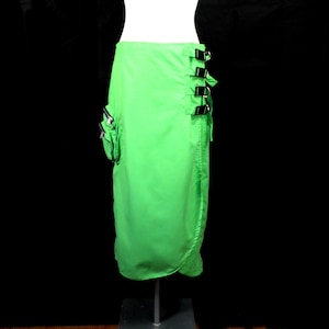 May include: A bright green skirt with a wrap-around design and multiple black buckles on the side. The skirt has a zippered pocket on the left side.