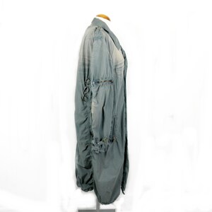 May include: A long, gray, lightweight jacket with a zipper closure and multiple pockets. The jacket has a distressed look and features decorative metal rings on the sleeves.