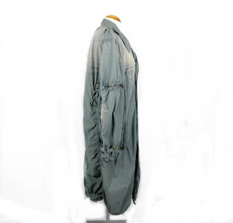May include: A long, gray, lightweight jacket with a zipper closure and multiple pockets. The jacket has a distressed look and features decorative metal rings on the sleeves.