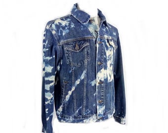 May include: A blue denim jacket with a unique bleach-dye pattern. The jacket features a classic design with a button-up front, chest pockets, and a collared neckline. The bleach effect creates a striking contrast against the dark denim.