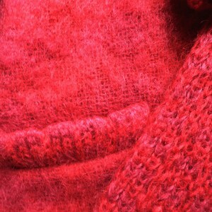 May include: Close-up of a red fuzzy knitted fabric with a seam running horizontally across the image.