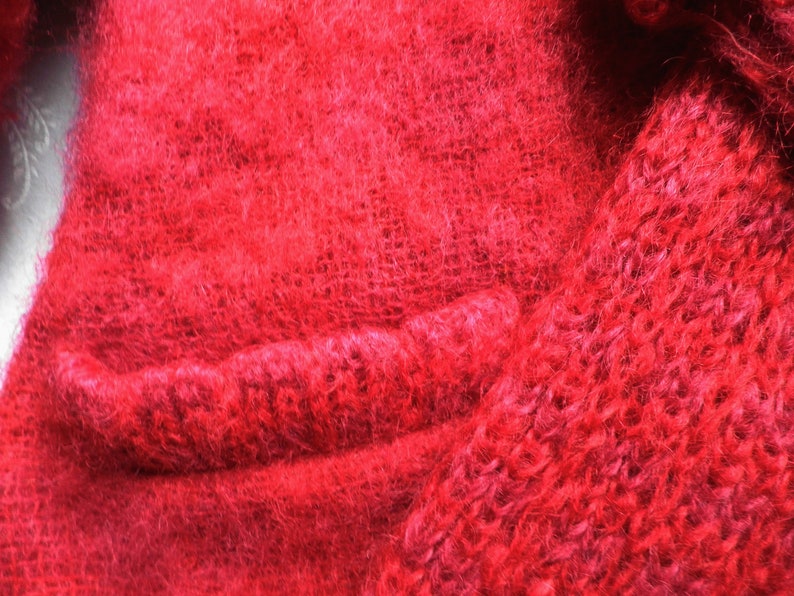 May include: Close-up of a red fuzzy knitted fabric with a seam running horizontally across the image.