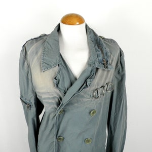 May include: A double-breasted, light green jacket with a zipper closure and a buckle detail on the front. The jacket has a distressed look and is made of a soft, cotton fabric.