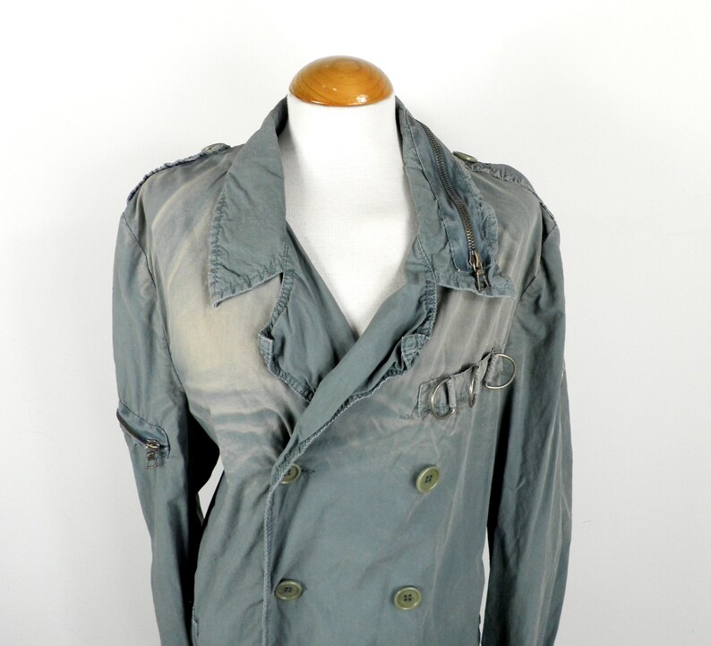 May include: A double-breasted, light green jacket with a zipper closure and a buckle detail on the front. The jacket has a distressed look and is made of a soft, cotton fabric.