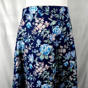 Pode incluir: Uma saia azul marinho com estampa floral com flores rosa, azuis e verdes. A saia tem uma silhueta reta e um comprimento na altura da panturrilha.