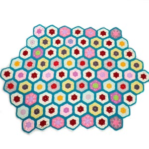 May include: A crocheted blanket with a honeycomb pattern in shades of pink, red, yellow, green, and blue. The blanket is made of yarn and has a teal border.
