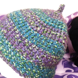 May include: A purple, green and white knitted hat with a pointed top.
