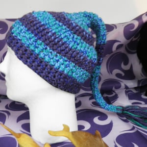 May include: A blue and purple striped crocheted hat with a long tail. The hat is on a mannequin head.