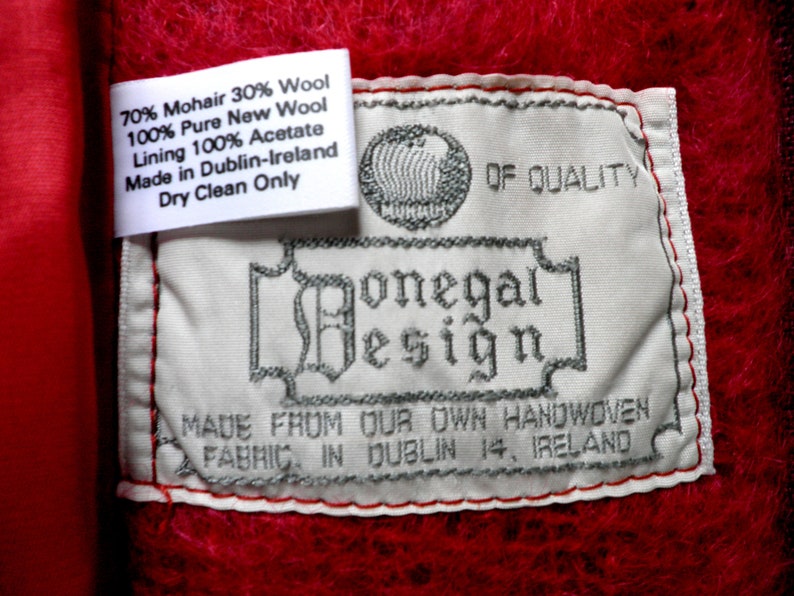 May include: White label with black text that reads "70% Mohair 30% Wool 100% Pure New Wool Lining 100% Acetate Made in Dublin-Ireland Dry Clean Only" and a larger label with black text that reads "OF QUALITY Donegal Design MADE FROM OUR OWN HANDWOVEN FABRIC IN DUBLIN 14, IRELAND".
