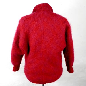 May include: A red fuzzy sweater with a high neck and long sleeves.
