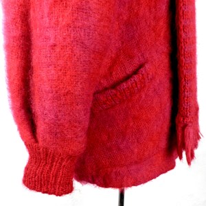 May include: A fuzzy red cardigan with a pocket on the left side and a fringed edge on the right side.