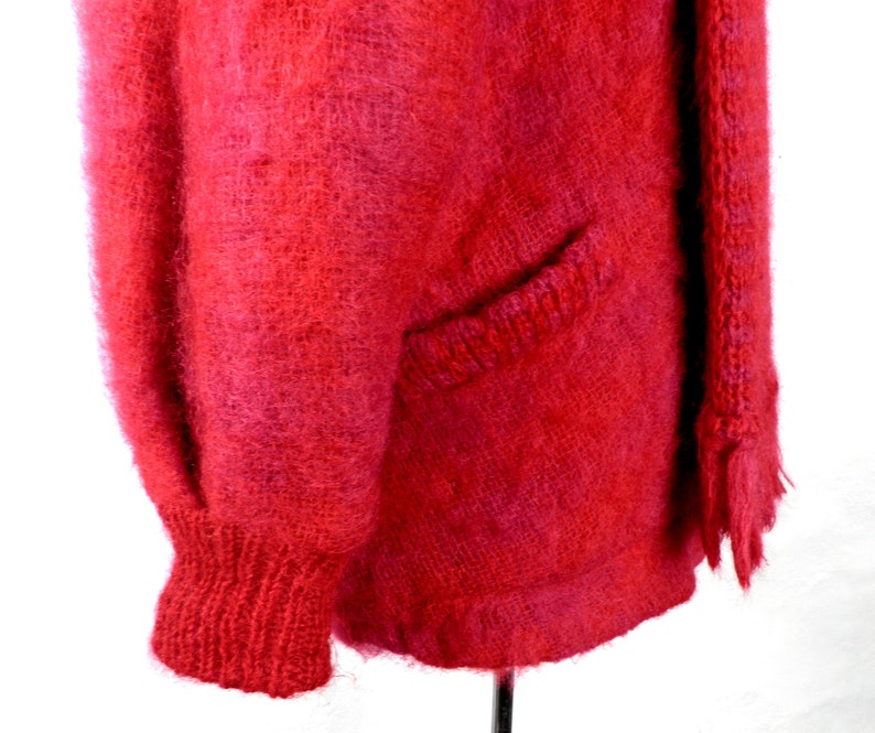 May include: A fuzzy red cardigan with a pocket on the left side and a fringed edge on the right side.