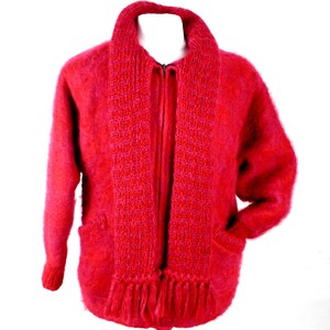 May include: A red fuzzy cardigan with a matching scarf. The cardigan has a zipper closure and two pockets. The scarf has a fringe trim.