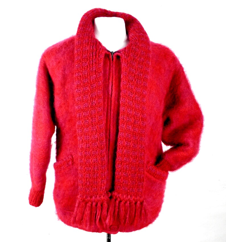 May include: A red fuzzy cardigan with a matching scarf. The cardigan has a zipper closure and two pockets. The scarf has a fringe trim.