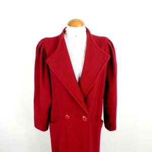 Può includere: Un lungo cappotto di lana rosso con chiusura a doppio petto e grandi tasche. Il cappotto ha un collo largo e maniche a sbuffo.