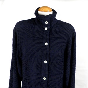 May include: A dark blue long-sleeved shirt with a textured, abstract pattern. The shirt has a high collar and a button-up front.