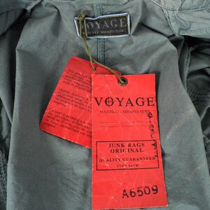 May include: Red and white label with the text "Voyage Mazilli - Michielsens Junk Rags Original Quality Guaranteed Turn Back A6509". The label is attached to a gray fabric with the text "Voyage Mazilli - Michielsens" on a smaller label.