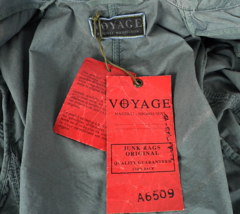 May include: Red and white label with the text "Voyage Mazilli - Michielsens Junk Rags Original Quality Guaranteed Turn Back A6509". The label is attached to a gray fabric with the text "Voyage Mazilli - Michielsens" on a smaller label.