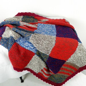 May include: A patchwork knitted throw blanket with a burgundy crocheted border. The blanket is made of squares in shades of red, blue, gray, and brown.