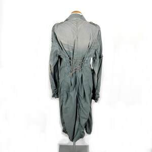 May include: A long, gray, cotton jacket with a lace-up back detail. The jacket has a collar and long sleeves.